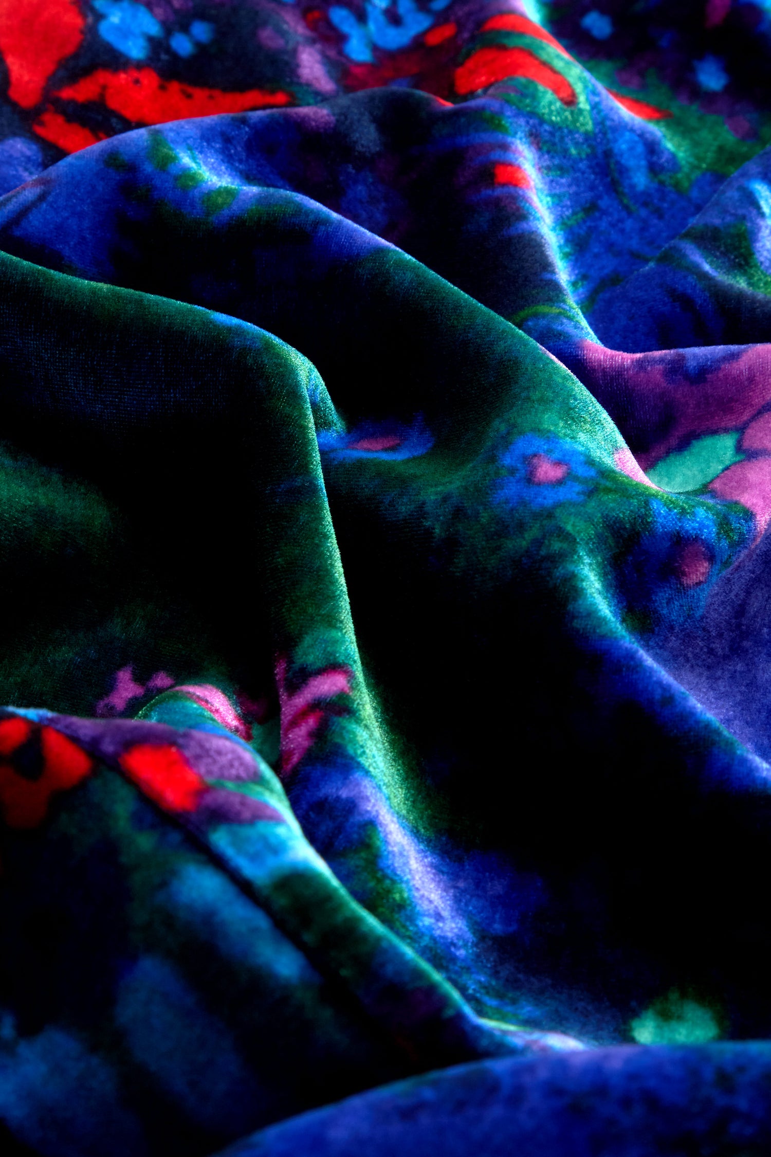 A close-up of the Late Night Flora Velvet Bubble Dress reveals its vibrant, multi-colored velvet fabric with a floral print, featuring draped soft folds in shades of blue, green, red, and purple—ideal for crafting an elegant evening look.