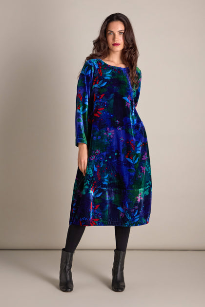 A woman in the Late Night Flora Velvet Bubble Dress, with its vibrant floral print and long sleeves, pairs it with black leggings and ankle boots while standing gracefully against a plain background.