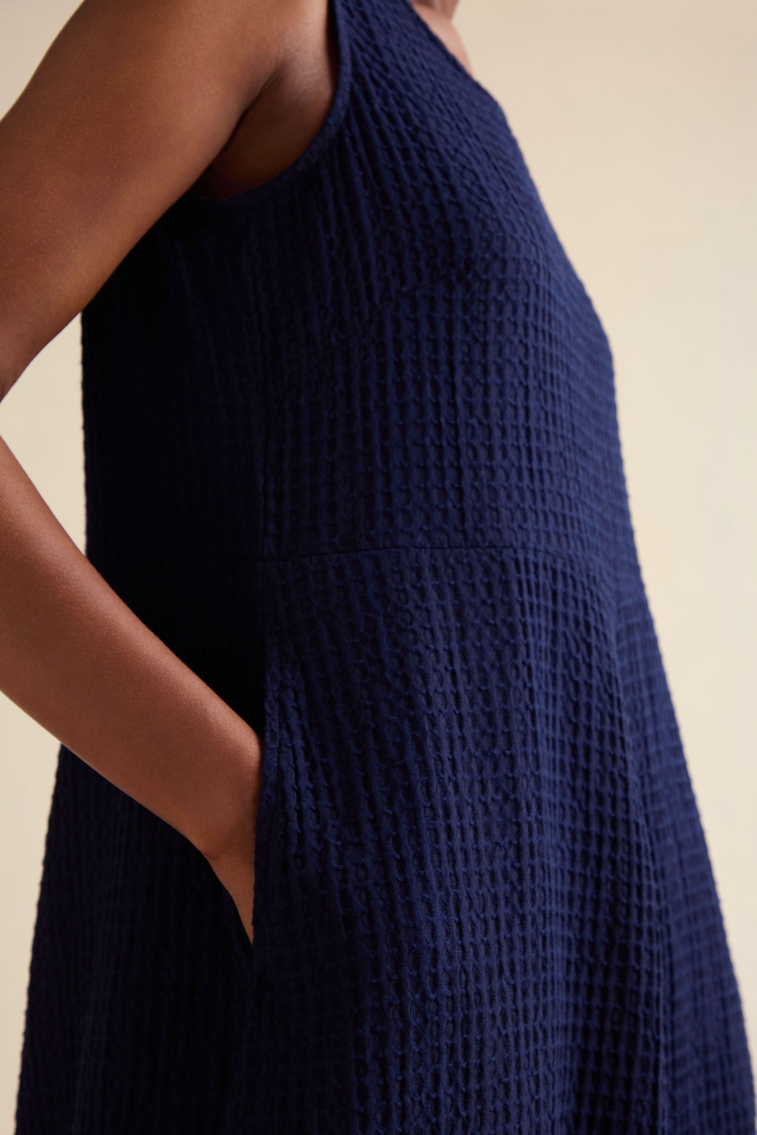 Close-up of a person wearing the Mini Waffle Cotton Bubble Dress in navy blue, featuring a sleeveless design, textured weave, midi length, and side pocket detail.