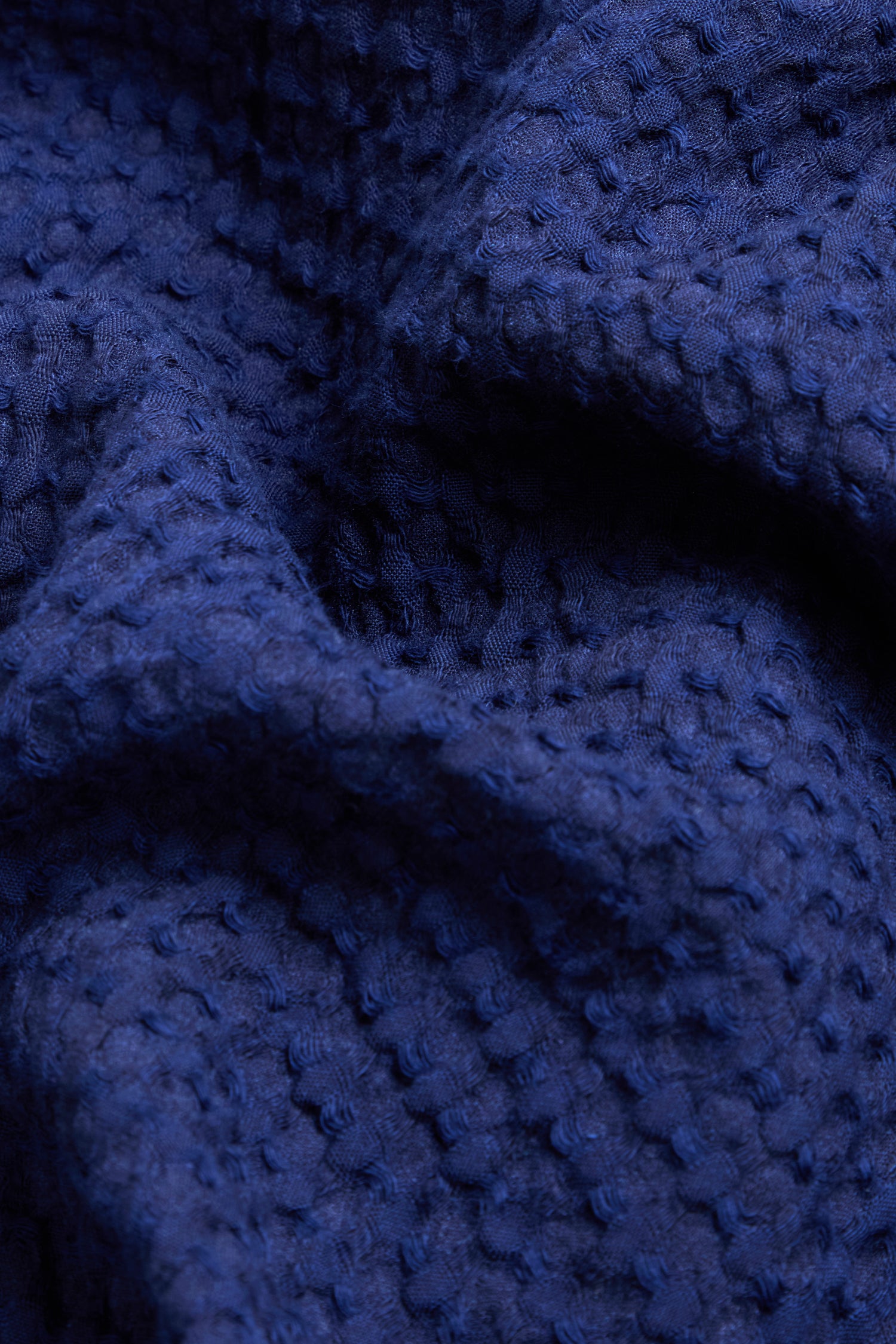 Close-up of textured blue fabric with a waffle-like pattern and visible folds, similar to the material featured in the Mini Waffle Cotton Bubble Dress.