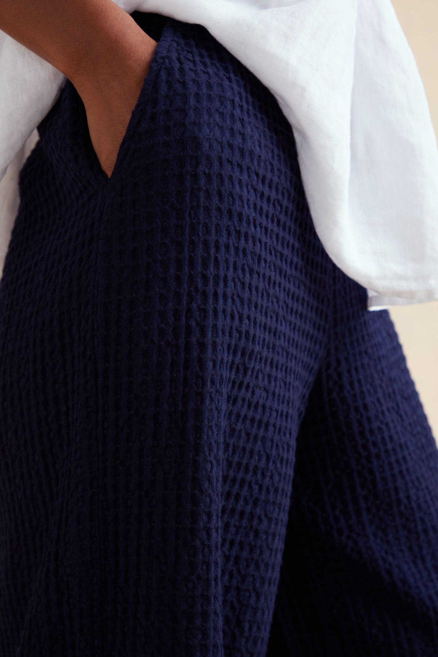Person wearing the Mini Waffle Cotton Bubble Trouser in navy blue with a hand in the pocket, paired with a loose white top. These cropped cotton trousers feature subtle textured detailing for added style.