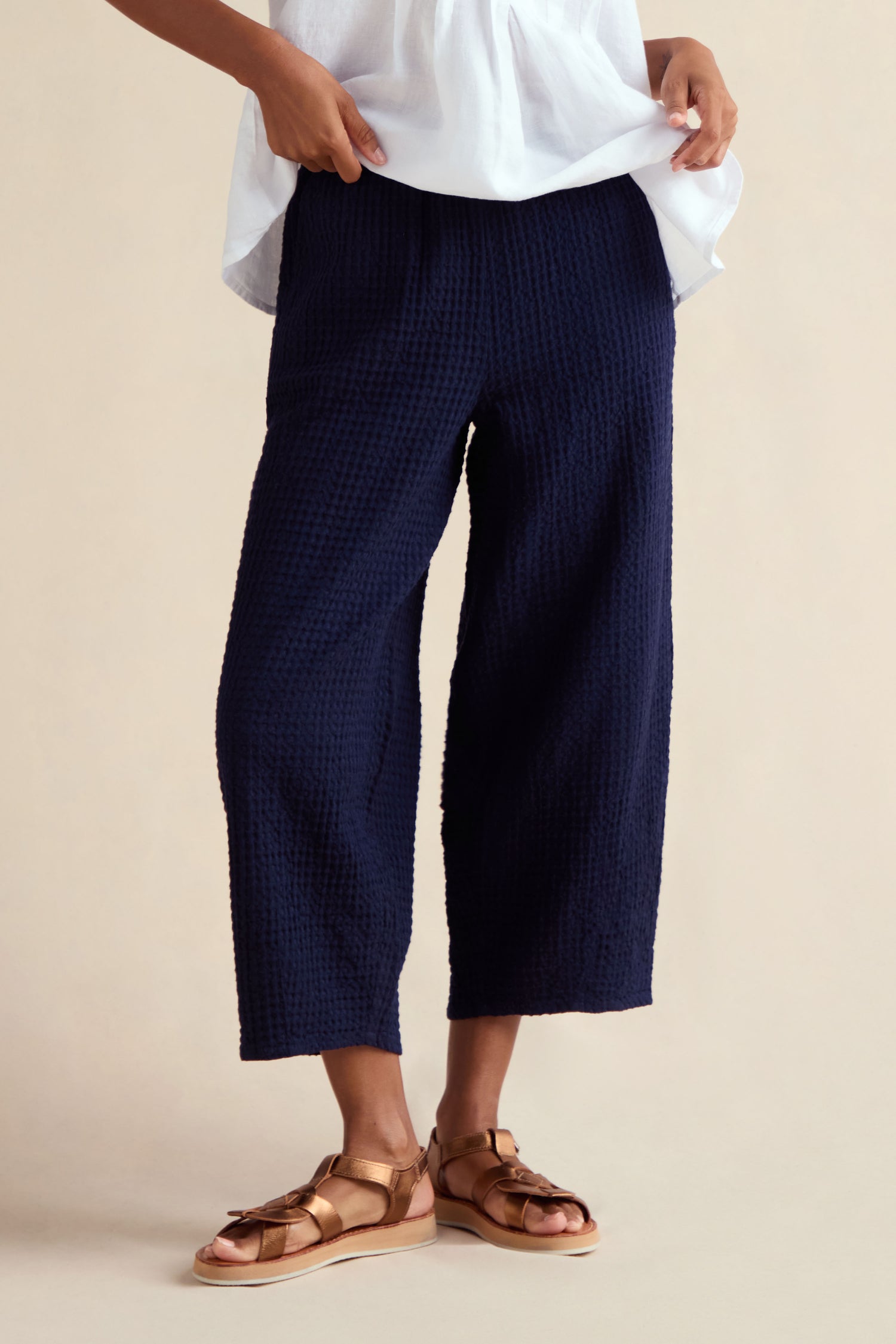 Person wearing Mini Waffle Cotton Bubble Trouser in navy, paired with a white top and tan sandals, standing against a neutral background. Only the lower half of the body is visible.