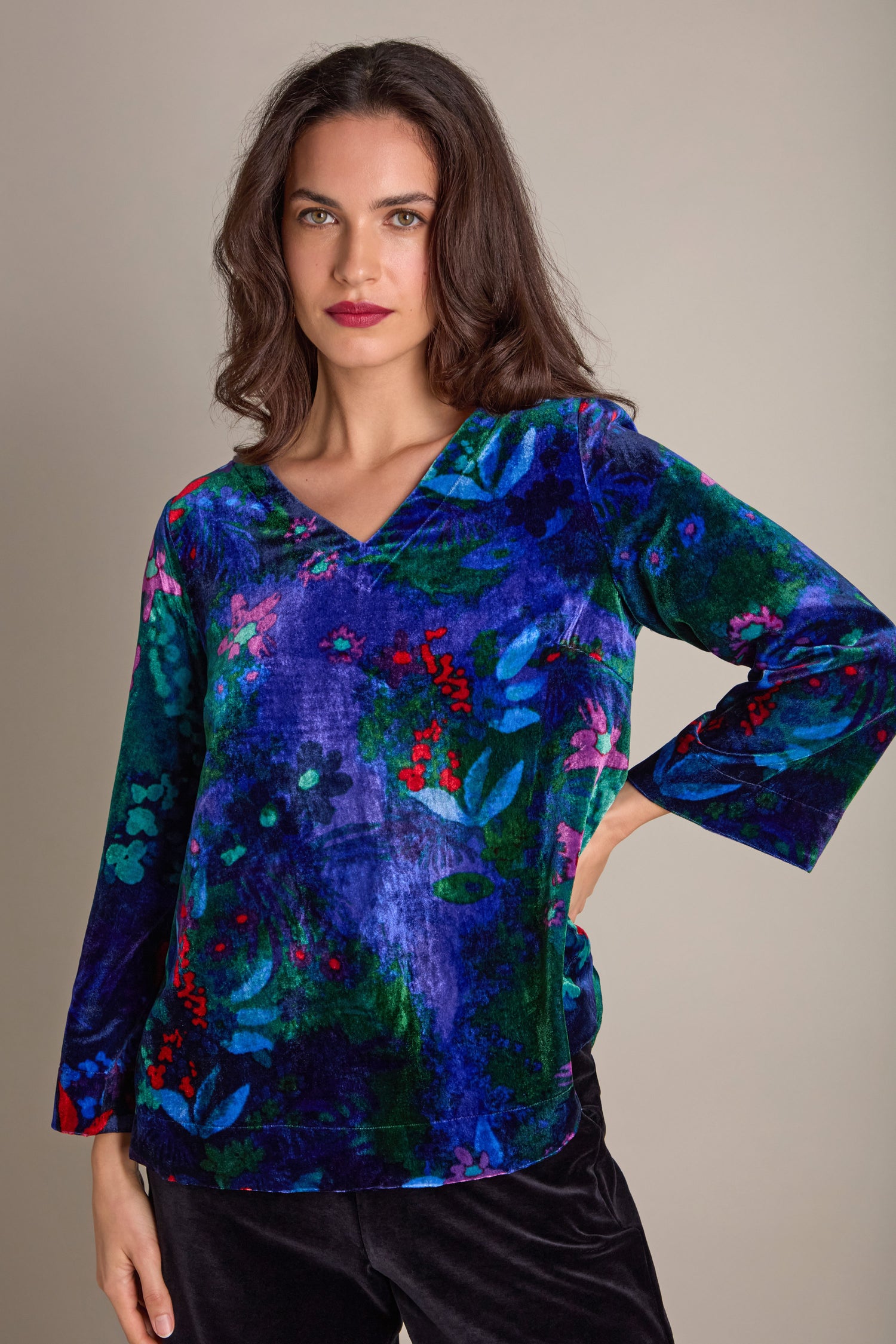 A woman wears the Late Night Flora Velvet Top, showcasing an A-line style adorned with jewel-toned blue and green floral prints on a neutral backdrop.