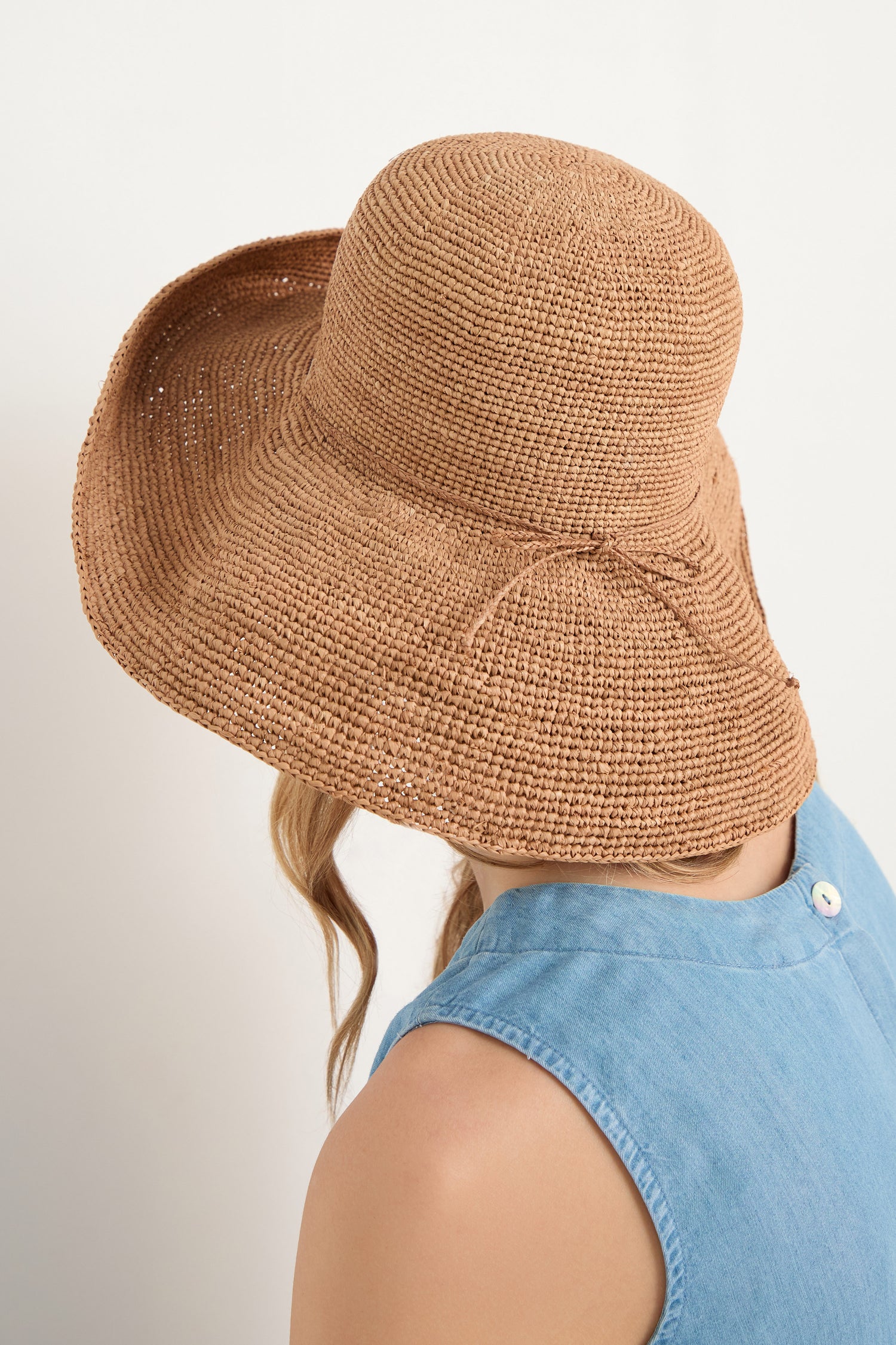 A person faces away from the camera, wearing a Handwoven Raffia Tie Hat with a wide brim and a sleeveless light blue top.