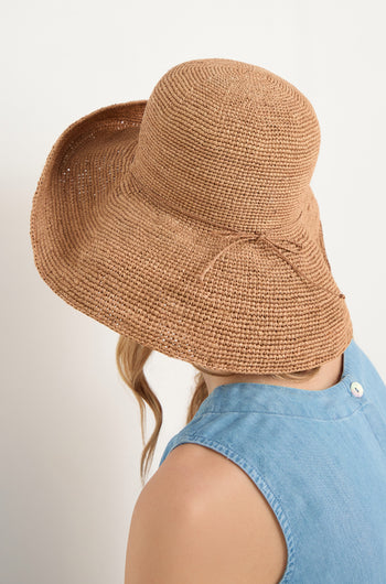 A person faces away from the camera, wearing a Handwoven Raffia Tie Hat with a wide brim and a sleeveless light blue top.