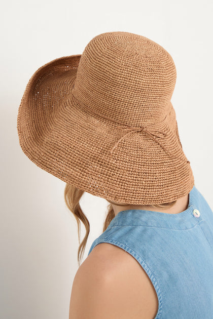 A person faces away from the camera, wearing a Handwoven Raffia Tie Hat with a wide brim and a sleeveless light blue top.