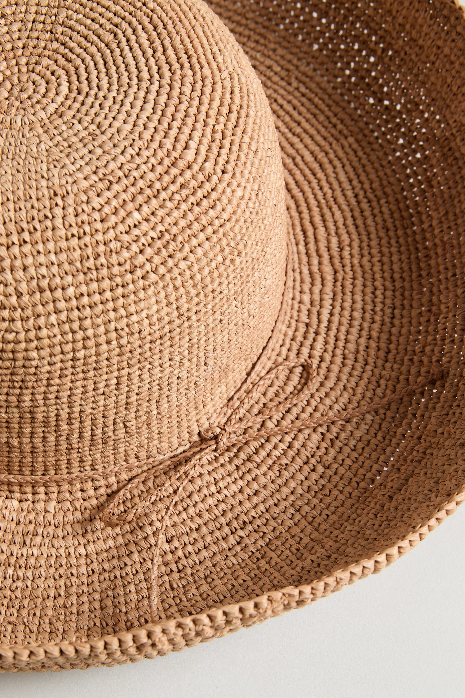 A close-up of the Handwoven Raffia Tie Hat, featuring a wide brim and simple bow detail, displayed on a light background.