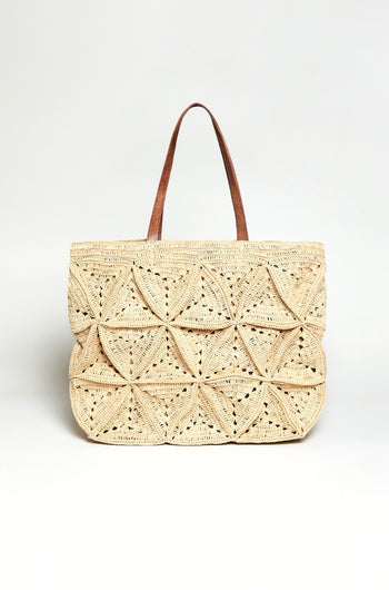 The Handwoven Raffia Basket Bag features geometric patterns and two brown handles, crafted by artisans in Madagascar. Displayed against a plain white background, it showcases intricate handwoven detail.