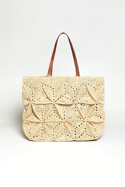 The Handwoven Raffia Basket Bag features geometric patterns and two brown handles, crafted by artisans in Madagascar. Displayed against a plain white background, it showcases intricate handwoven detail.
