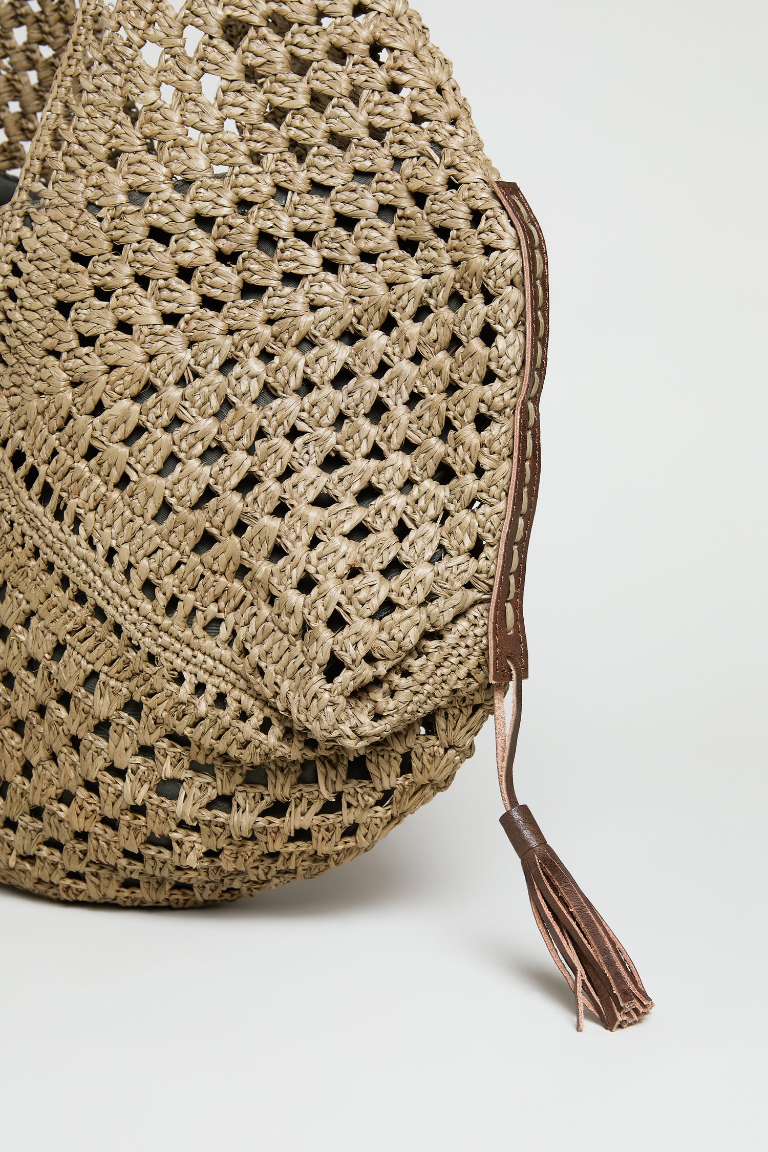 Close-up of a woven straw hat with a brown leather tassel detail, reminiscent of the Handwoven Raffia Tassel Detail Handbag from Madagascar, shown against a plain background.