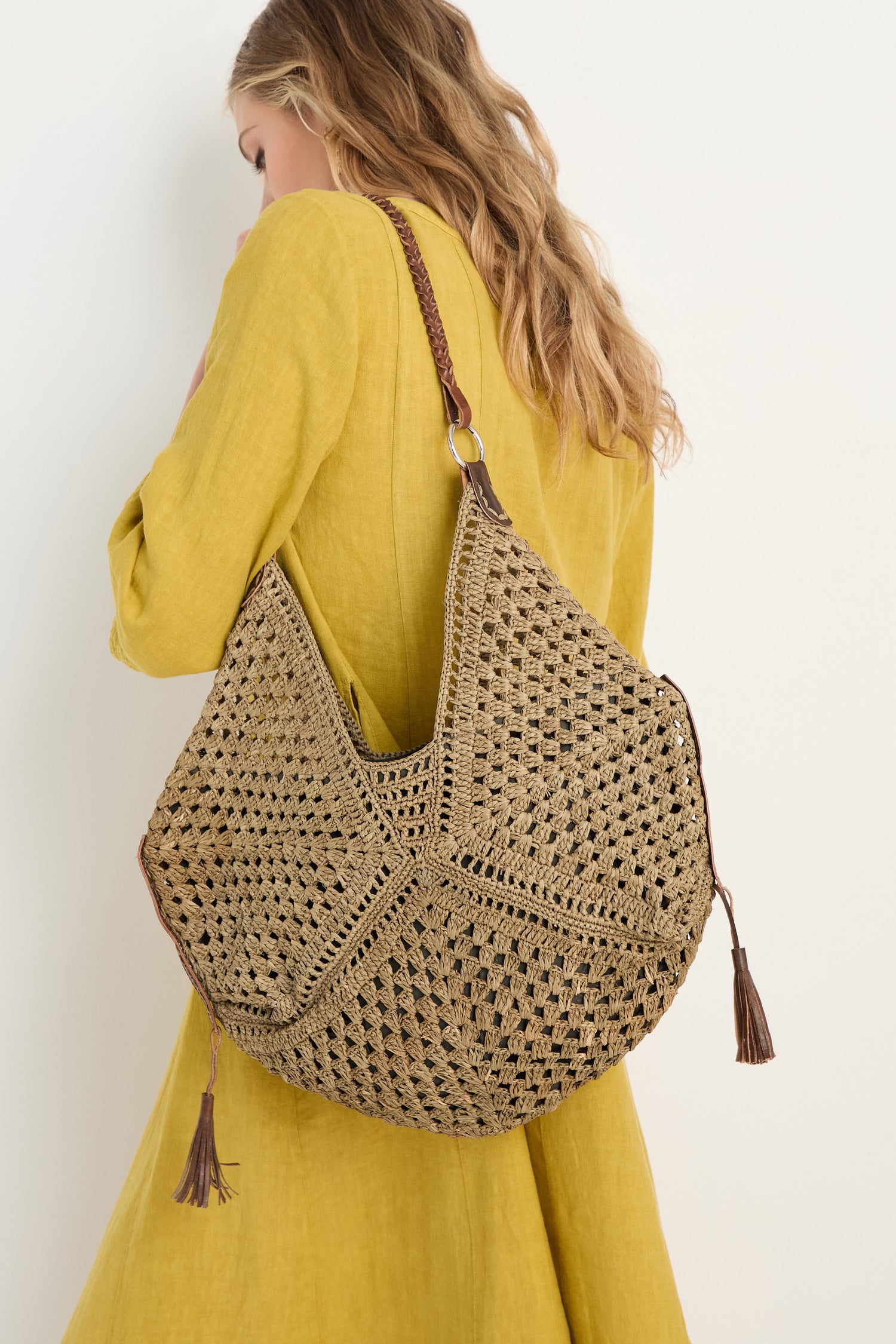 A woman in a yellow dress carries the Handwoven Raffia Tassel Detail Handbag, posing against a plain white background.