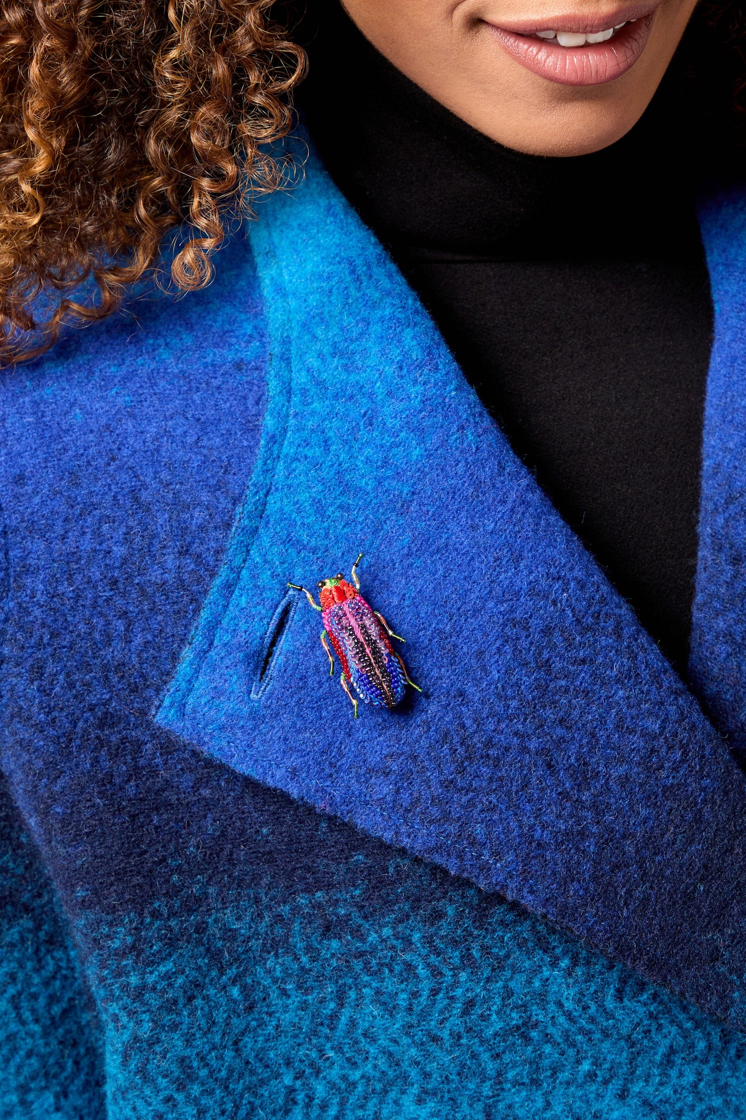 A woman wearing a blue coat with a Rainbow Leaf Beetle Brooch.