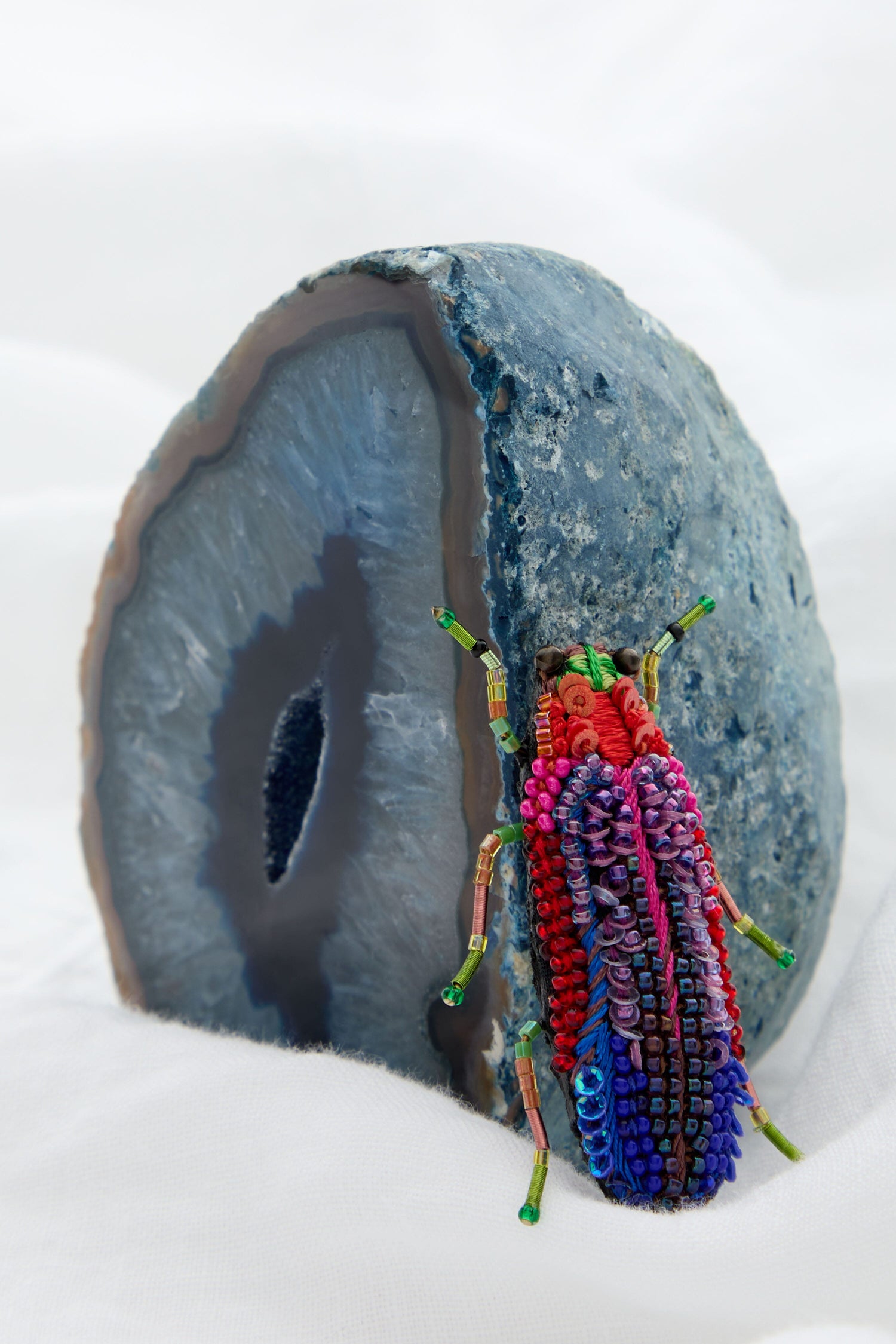 A Rainbow Leaf Beetle Brooch perched on top of a blue rock, resembling a beaded brooch.