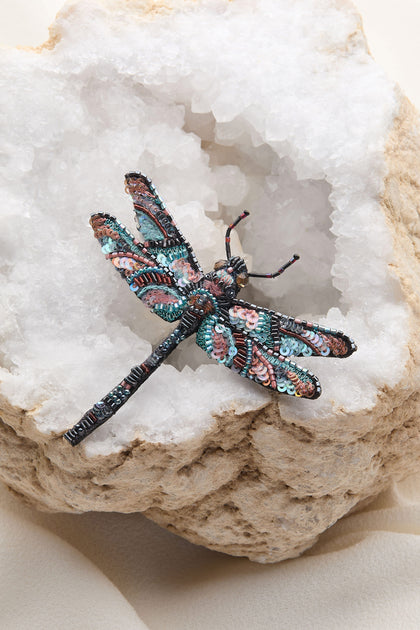 A Hand Beaded Sequin Dragonfly Brooch from Trovelore delicately rests on a white, crystalline rock formation.