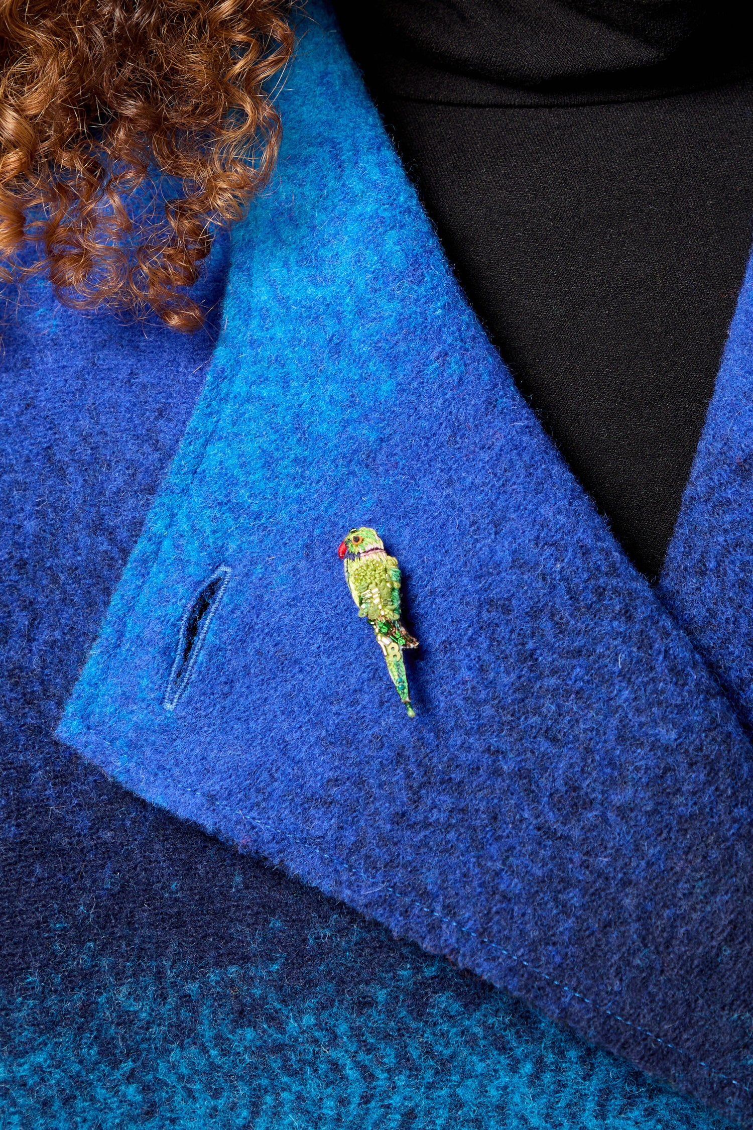 A woman wearing a blue jacket with a Hand Embroidered Parrot Brooch on it.