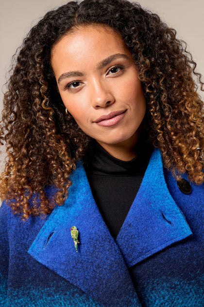 A woman wearing a blue and black coat with a Hand Embroidered Parrot Brooch.