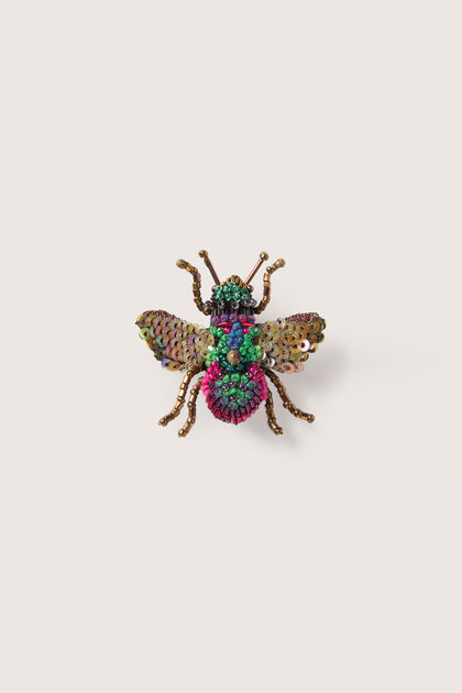 A vibrant Hand Beaded Sequin Rainbow Bee Brooch with detailed multicolored beadwork, including green, pink, and gold tones, on a plain beige background.