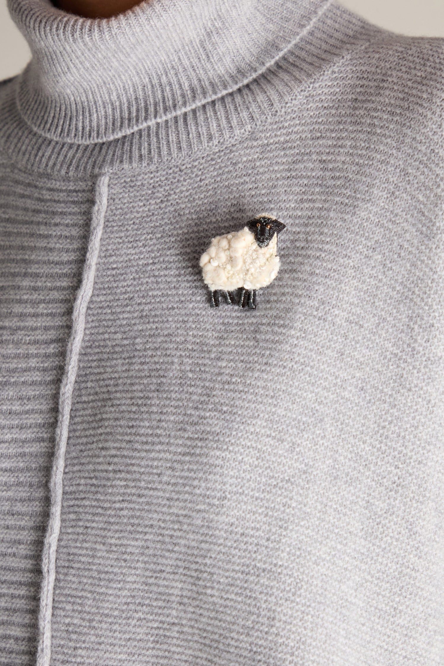 Close-up of a person wearing a gray turtleneck sweater with a Hand Embroidered Ewe Brooch attached on the left side of the chest.