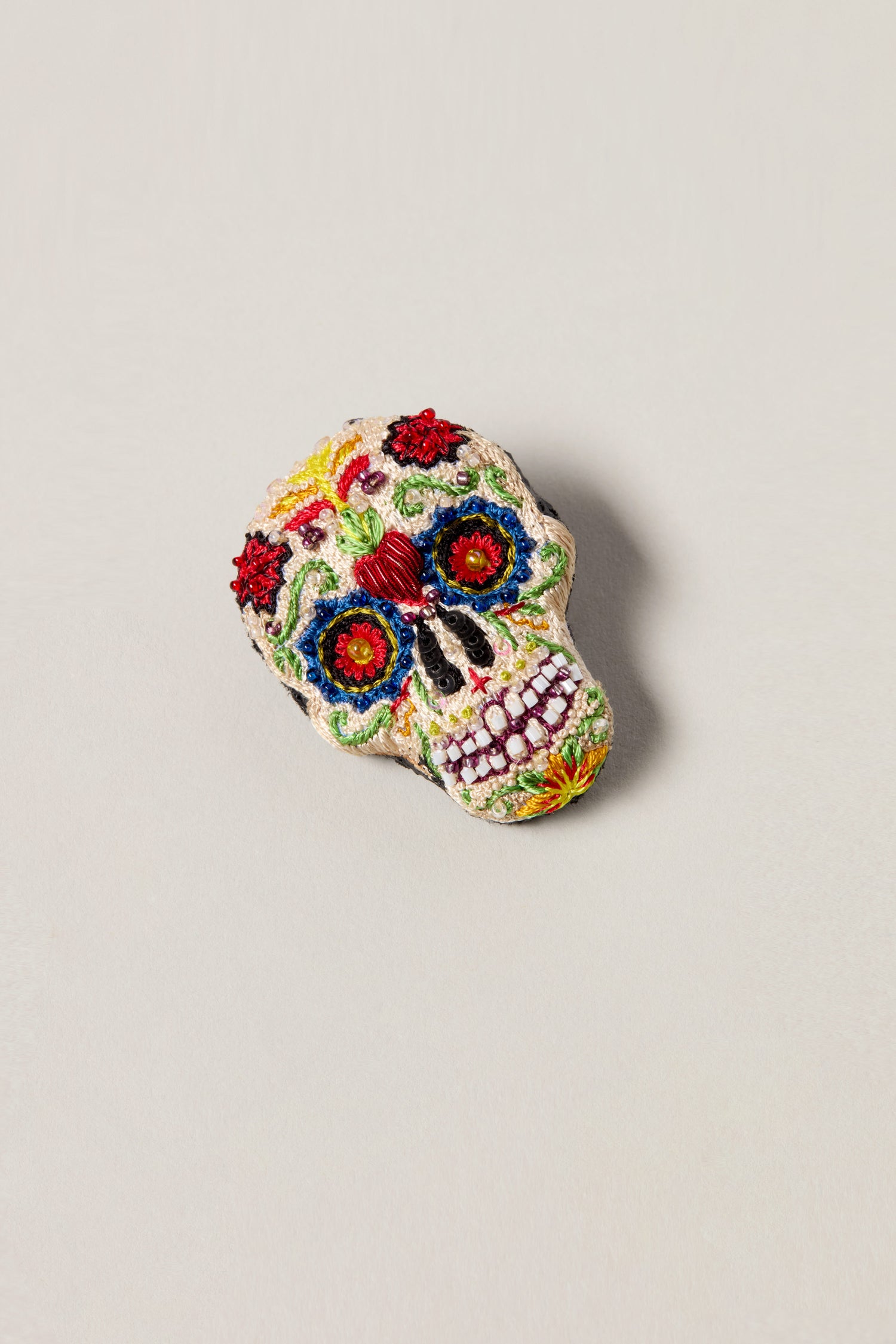 Hand Embroidered Calavera Brooch featuring colorful floral and decorative patterns, reminiscent of the Day of the Dead, displayed on a light, neutral background.