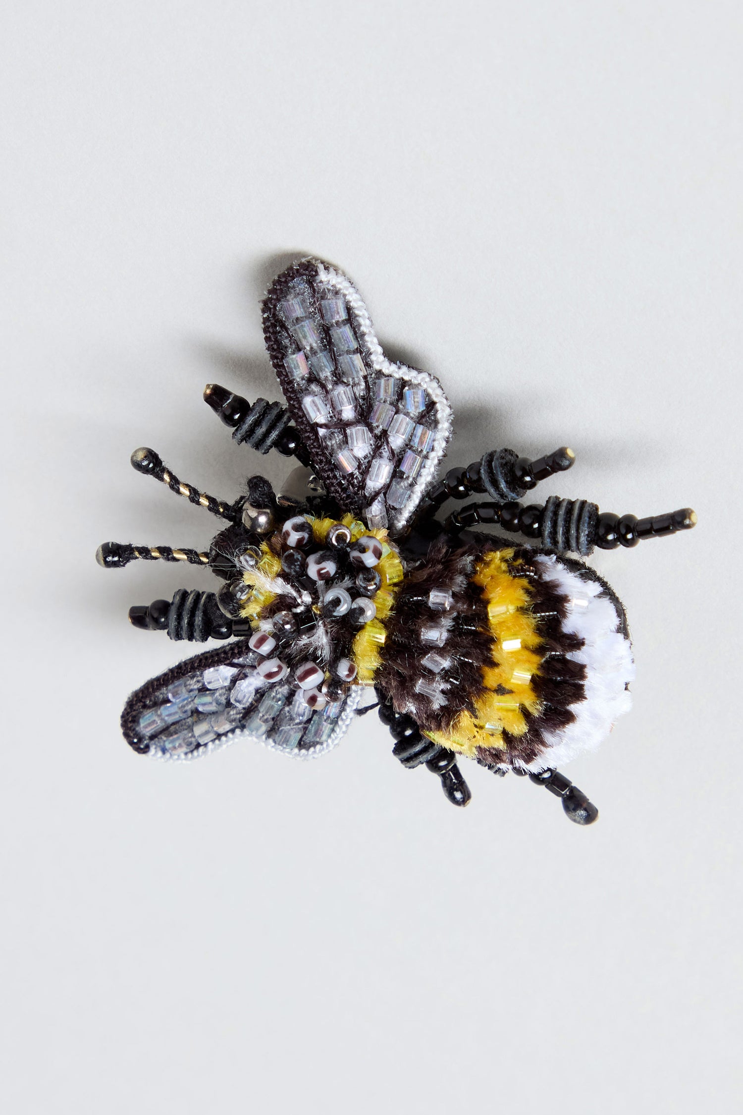 The Hand Beaded Yellow-Banded Bee Brooch is a beautifully hand embroidered accessory crafted in the shape of a bee, adorned with yellow, black, white, and silver beads meticulously arranged to depict its detailed wings and body. This elegant brooch captures the charming essence of the yellow-banded bee with exquisite detail.