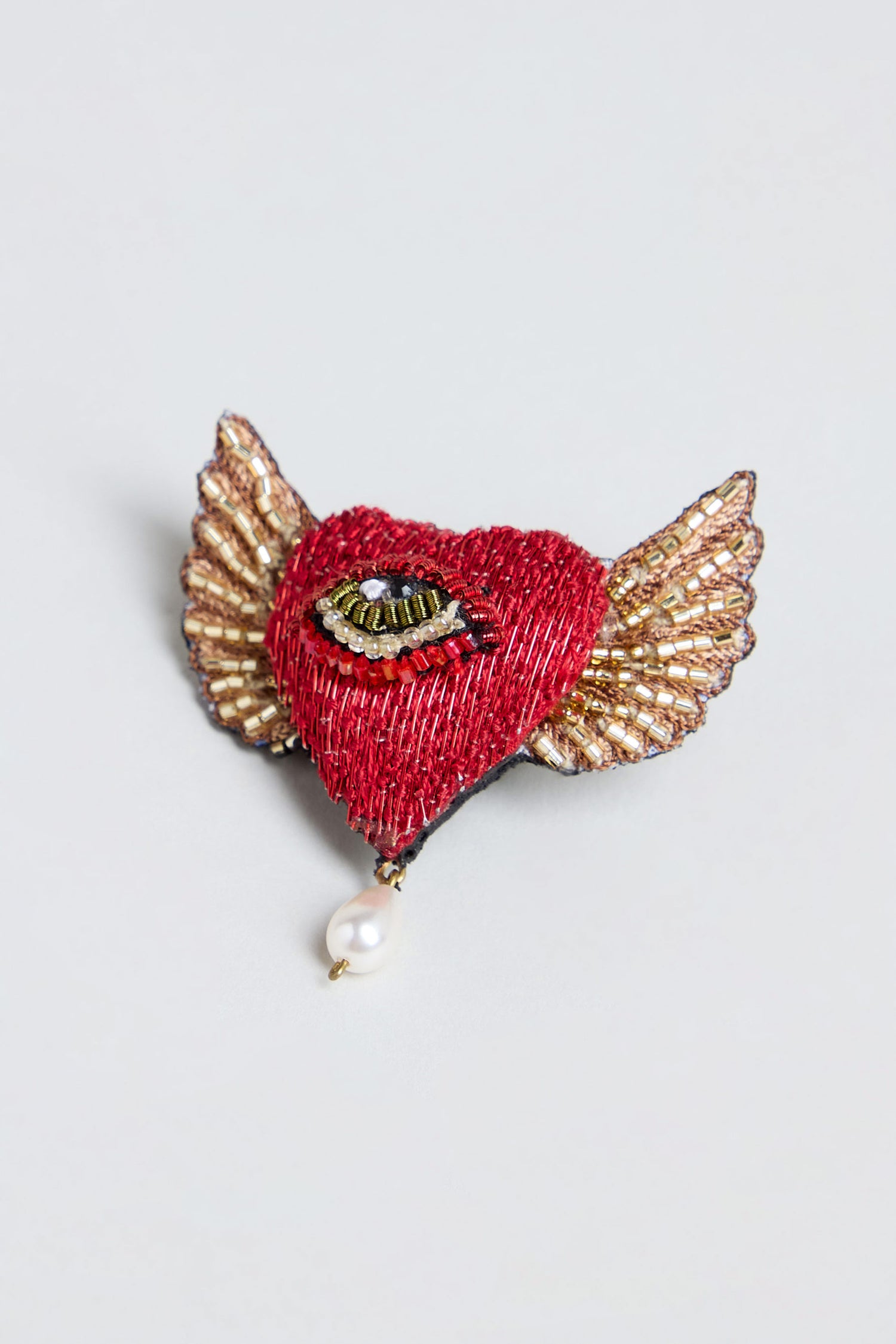 Introducing the Hand Beaded Guardian Heart Brooch—featuring a red, heart-shaped design with elegant gold wings, a meticulously hand-beaded eye at its center, and a single pearl delicately suspended from the bottom.
