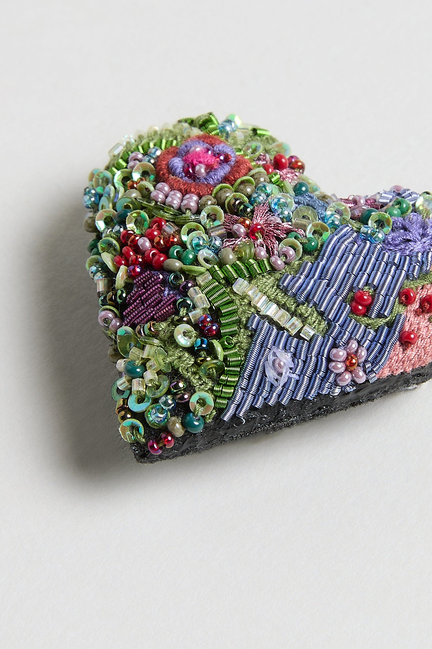 A close-up of the Hand Embroidered Blooming Heart Brooch, a heart-shaped accessory adorned with colorful beads, sequins, and detailed embroidery, shown on a light background.