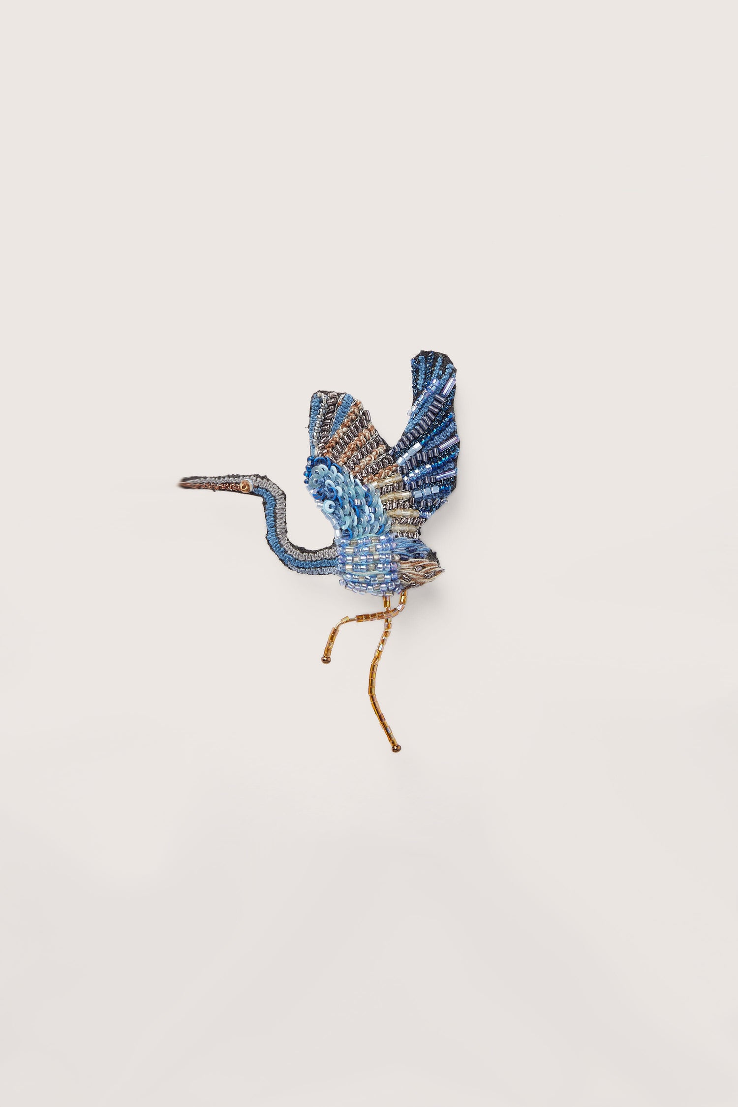 A stunning Hand Embroidered Blue Heron Brooch gracefully glides across a white wall.