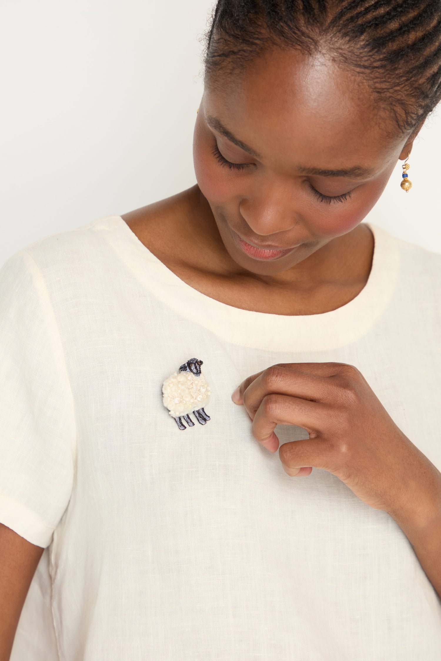 A woman in a white shirt gazes down, admiring the Hand Embroidered Sheep Brooch pinned to her chest.
