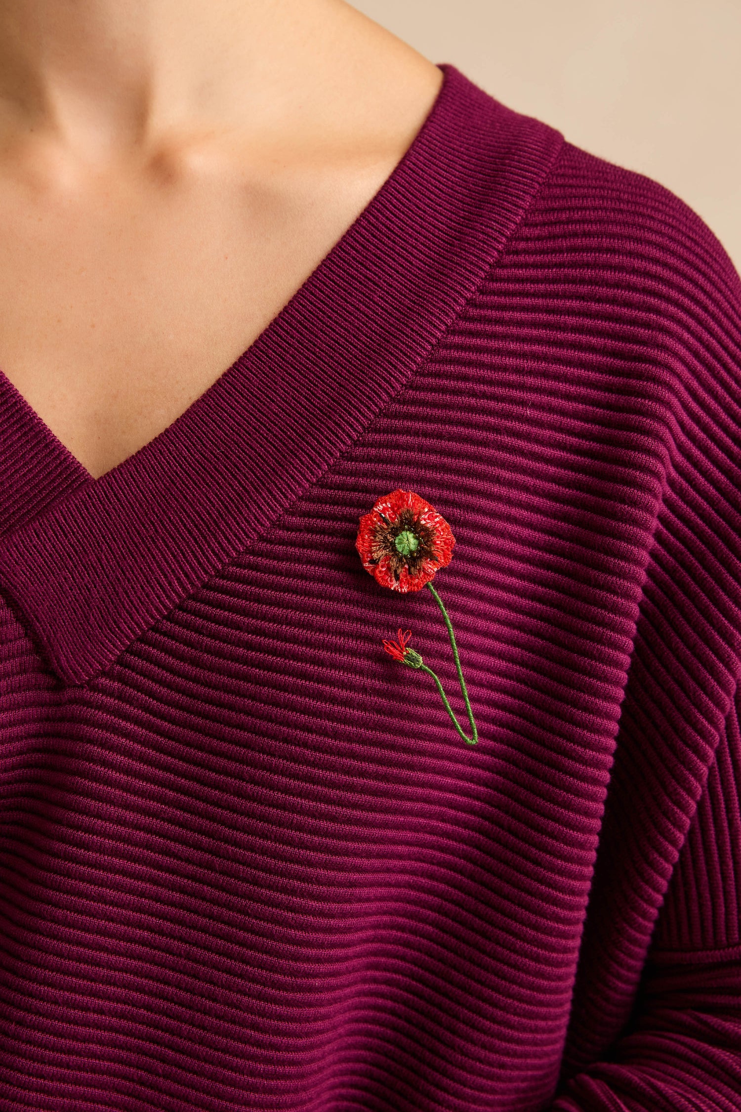 A person wears a ribbed, deep purple top adorned with the Hand Beaded Shirley Poppy Brooch—pinned near the neckline.