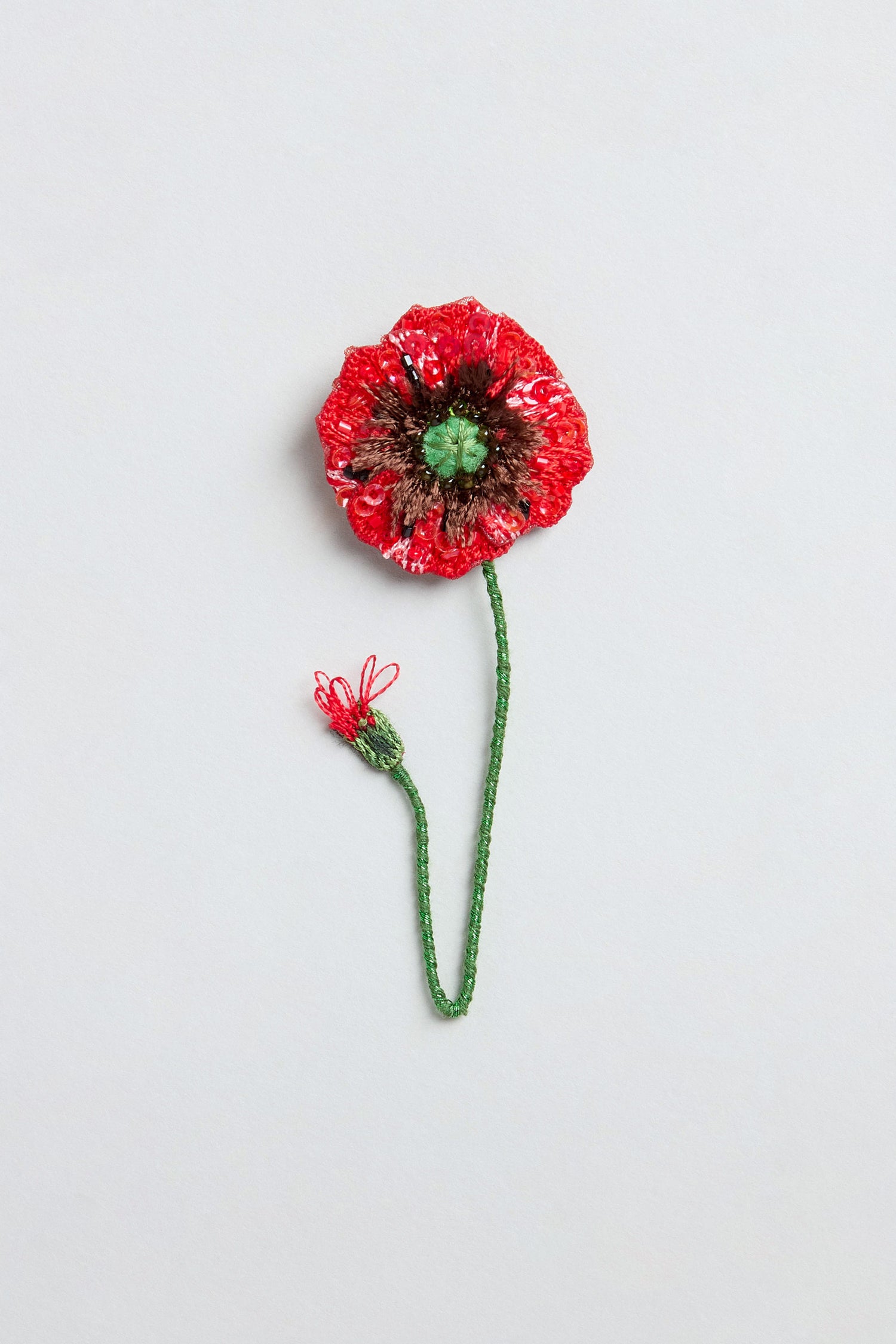 Illustration of a Hand Beaded Shirley Poppy Brooch featuring a vibrant red flower, green stem, and a small bud on a plain light background, highlighting the delicate details characteristic of hand embroidered brooch designs.