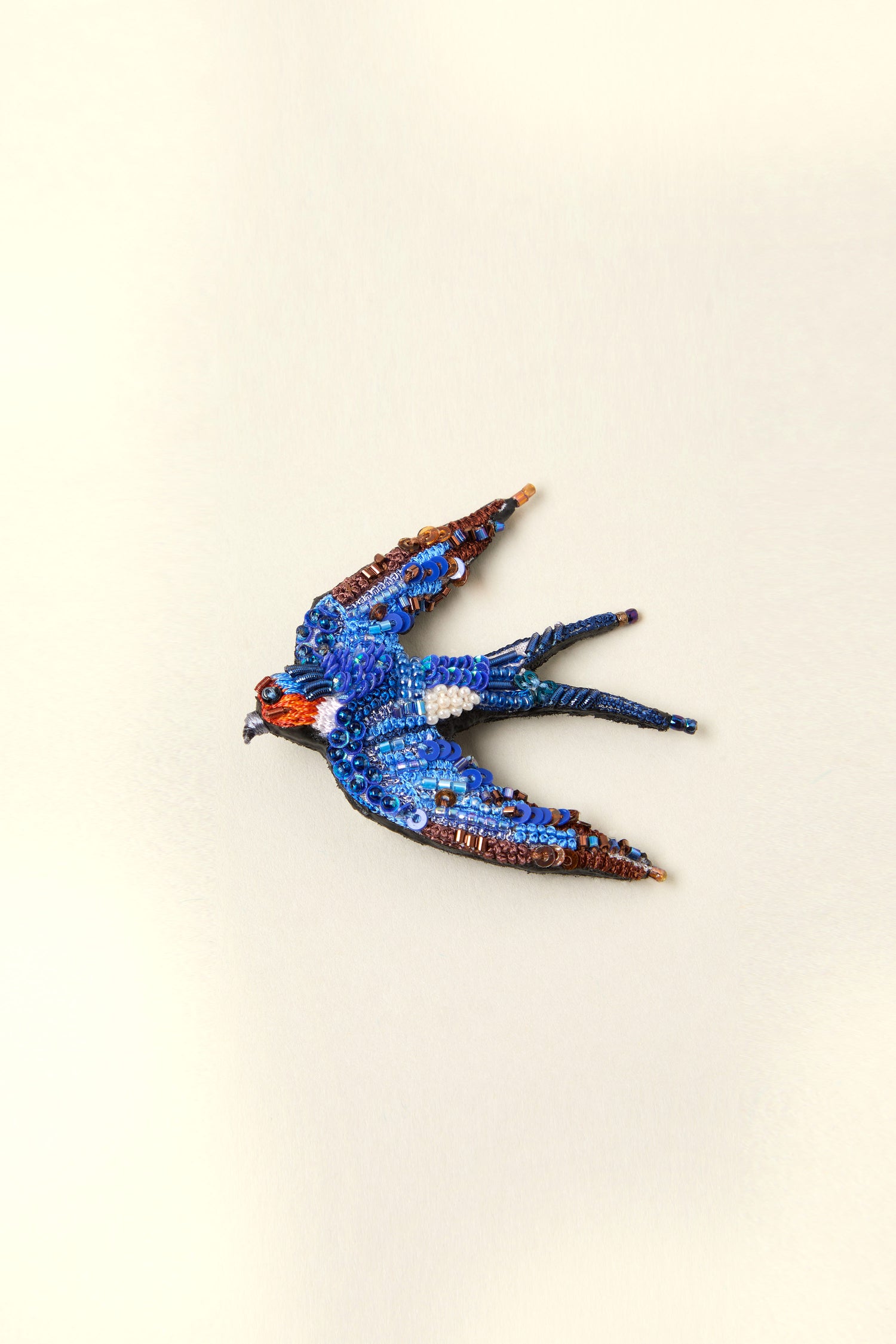 This Hand Beaded Flying Swallow Brooch is a sparkling masterpiece, showcasing an intricately beaded blue bird with outstretched wings. Its swallow shape brings the elegance and beauty of nature to life against a plain backdrop.