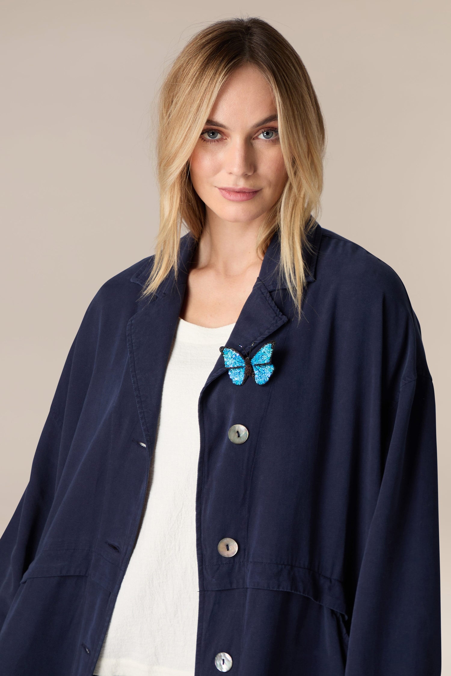 A woman wearing a blue jacket with a Hand Embroidered Morpho Butterfly Brooch.