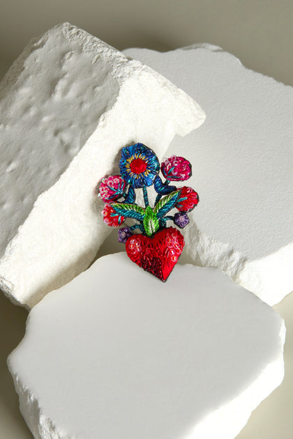 The Hand Beaded Flower Bouquet Brooch features colorful embroidery with a bright red heart and vibrant flowers on white textured stones.