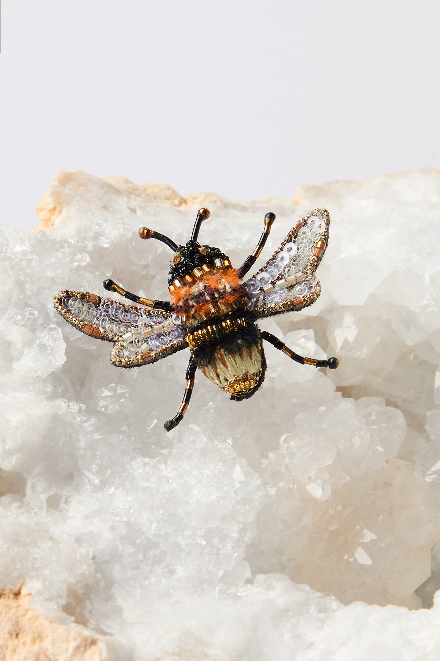 The Hand Beaded Humble Bee Brooch, an exquisite piece of hand embroidery, is elegantly displayed on a white crystalline rock, highlighting its sustainable design and intricate craftsmanship.