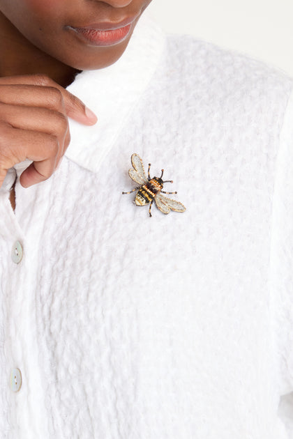 A person wears a textured white shirt with the Hand Embroidered Humble Bee Brooch pinned to the collar.