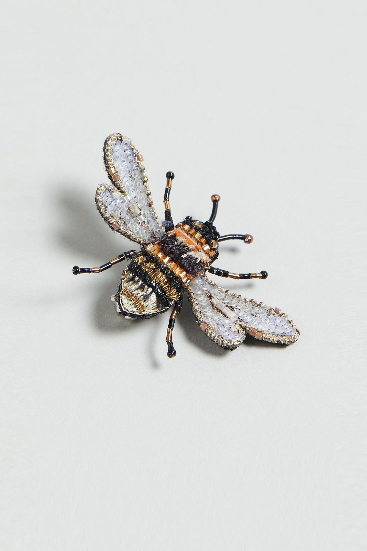 The Hand Embroidered Humble Bee Brooch features detailed gold, black, and white embroidery in the shape of a bee—a unique nature-inspired accessory for any collection.