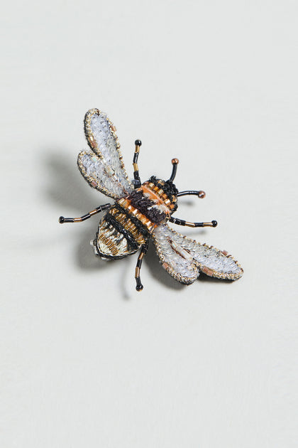 The Hand Embroidered Humble Bee Brooch features detailed gold, black, and white embroidery in the shape of a bee—a unique nature-inspired accessory for any collection.