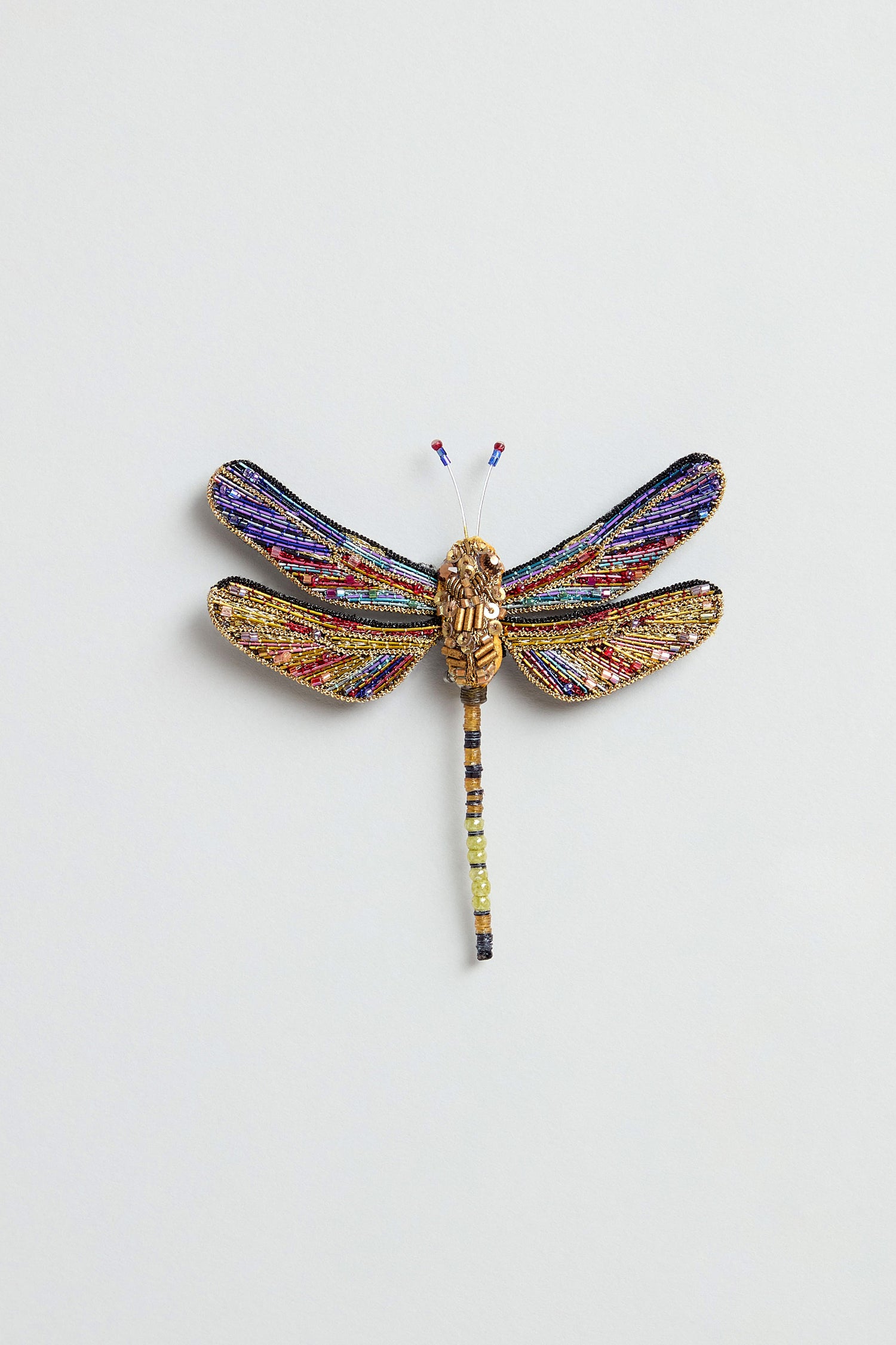 The Hand Beaded Hawker Dragonfly Brooch, featuring multicolored wings and a gold-toned body, is an exquisite piece of handmade jewelry displayed on a plain light background.