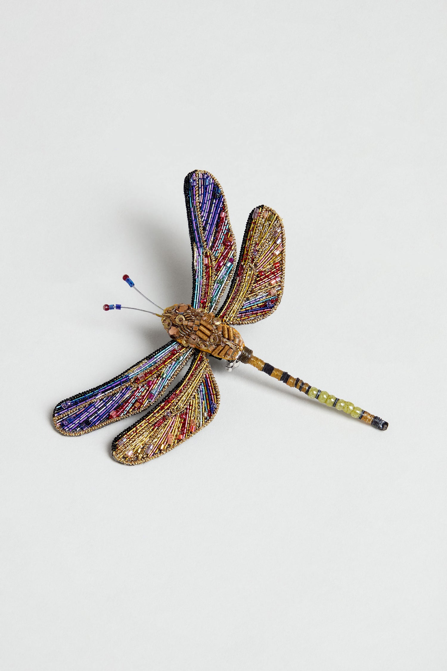 The Hand Beaded Hawker Dragonfly Brooch showcases four wings adorned with gold, purple, and red seed beads, a meticulously beaded body, and delicate wire antennae for an elegant decorative touch.