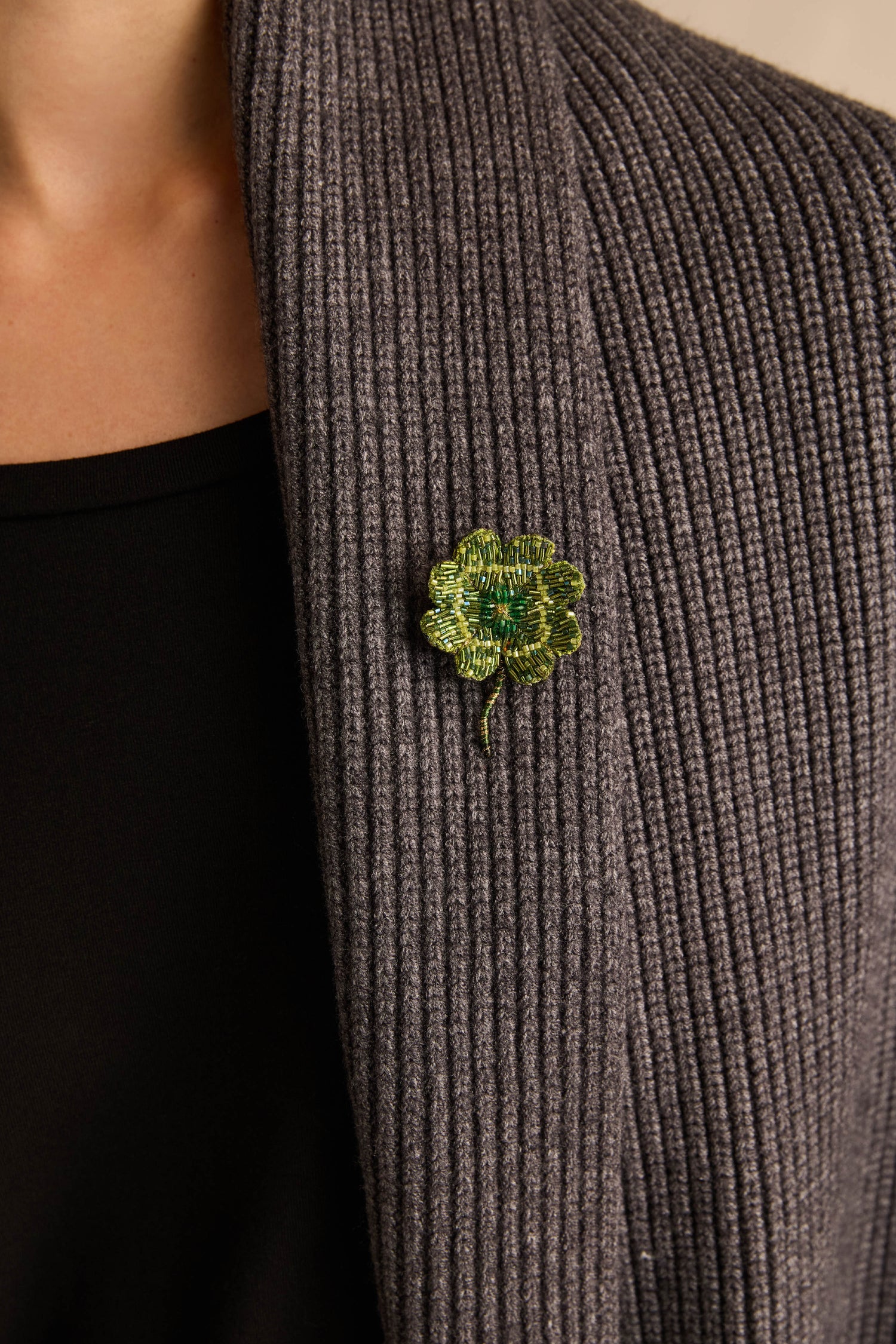 A person wearing a dark ribbed cardigan with the Hand Beaded Vintage Clover Brooch attached to the left side of the collar.