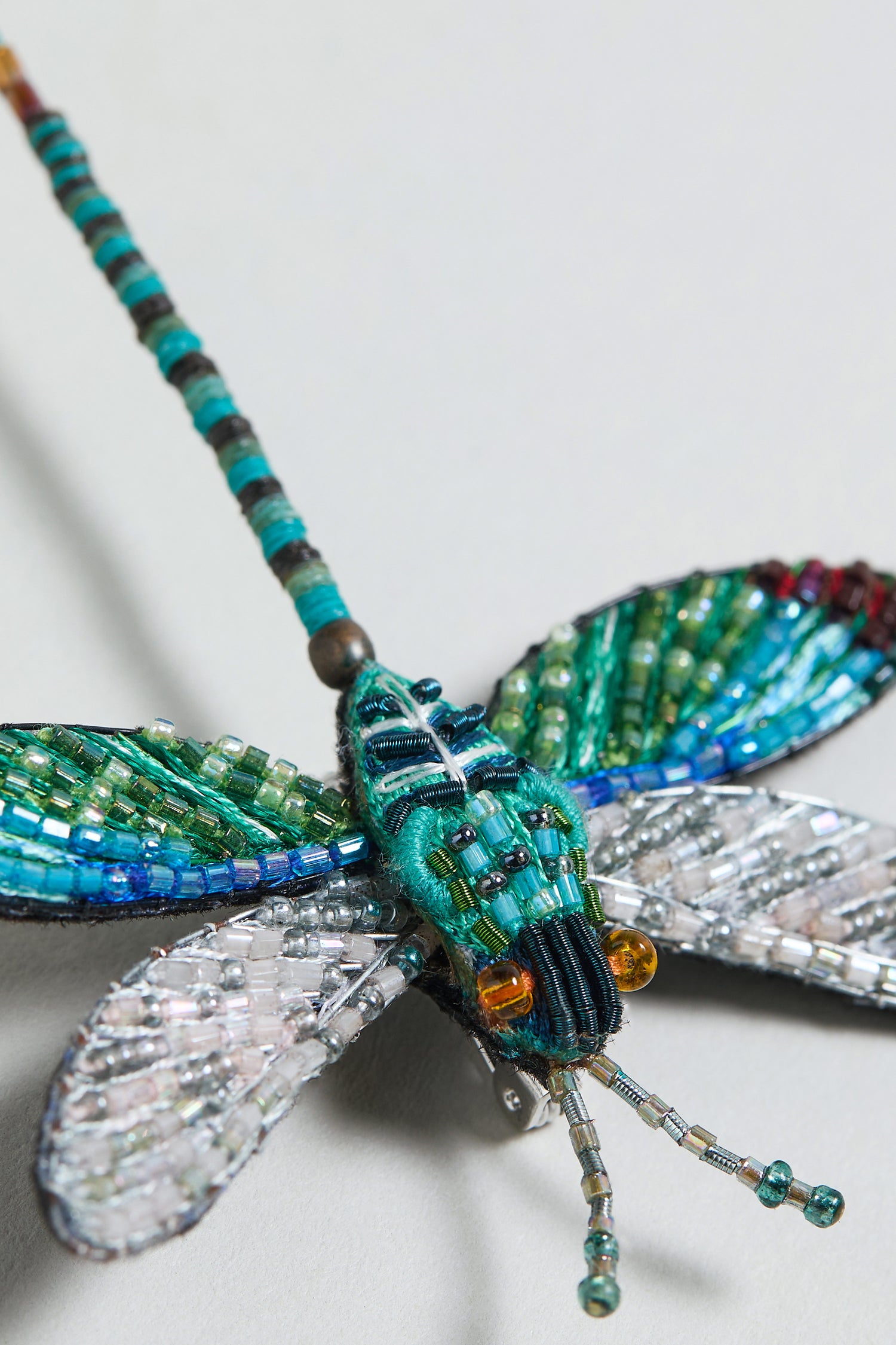 Close-up of the Hand Embroidered Oriental Greenwing Dragonfly Brooch, featuring blue, green, and silver beads on the wings and body, displayed against a light background.