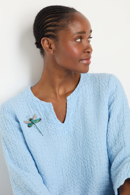 A woman in a textured light blue top wears the Hand Embroidered Oriental Greenwing Dragonfly Brooch, gazing to the side against a plain white background.