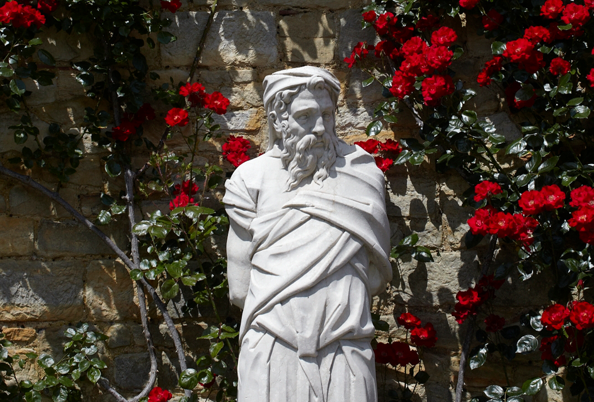 white statue of a man in front of some red flowers