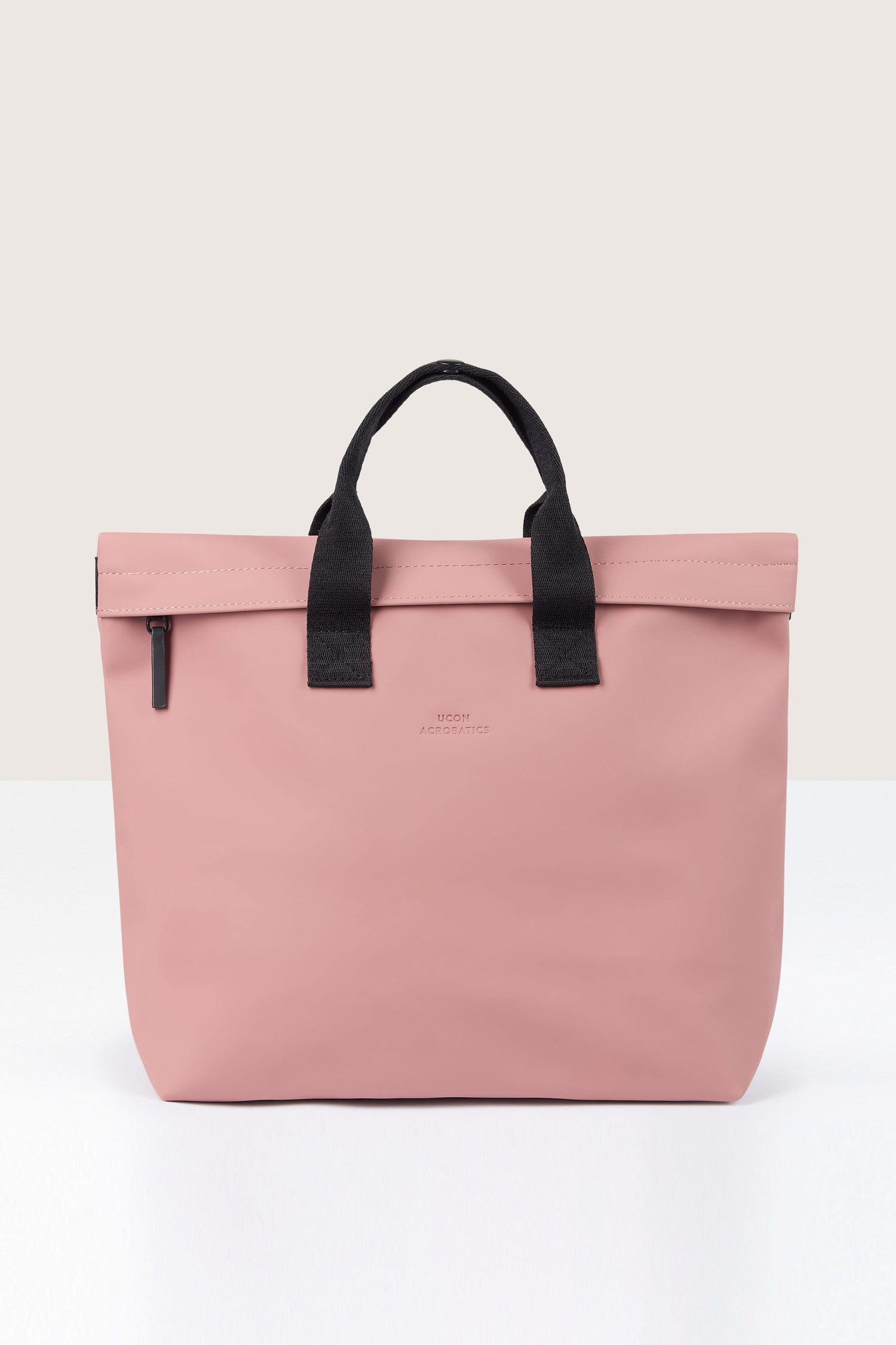 A pink Eliza Roll Top Backpack with black handles and a zipper, made from recycled PET bottles, is placed against a plain background.