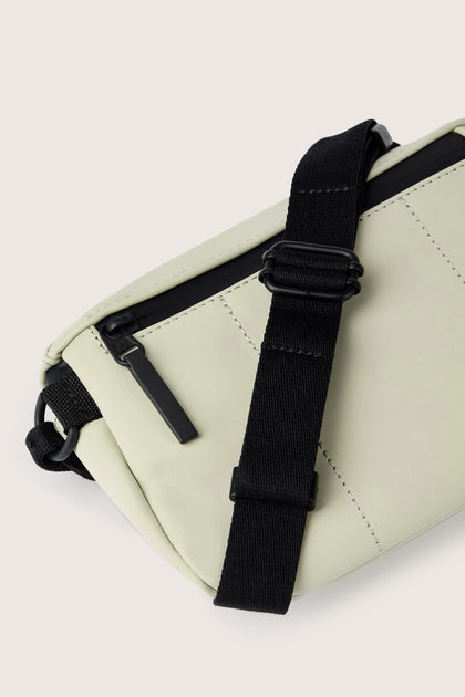 Close-up of the Jona Crossbody Bag, crafted from a sleek vegan tech material. This light-colored, water-repellent bag with black straps and a zipper pocket features simple stitching and a stylish design.