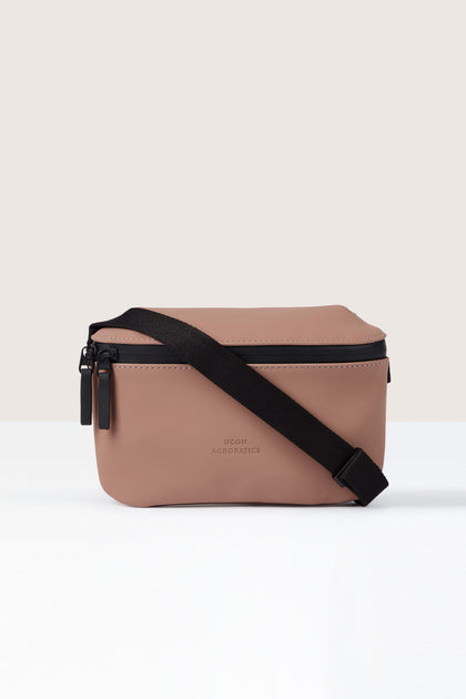 A small, pinkish-brown Jona Crossbody Bag crafted from water-repellent vegan tech material, with a black adjustable strap and the text "Ucon Acrobatics" on the front.