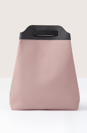 The Una Backpack features a minimalist pink bag with a black handle and top trim, crafted from recycled PET bottles, displayed against a neutral background.