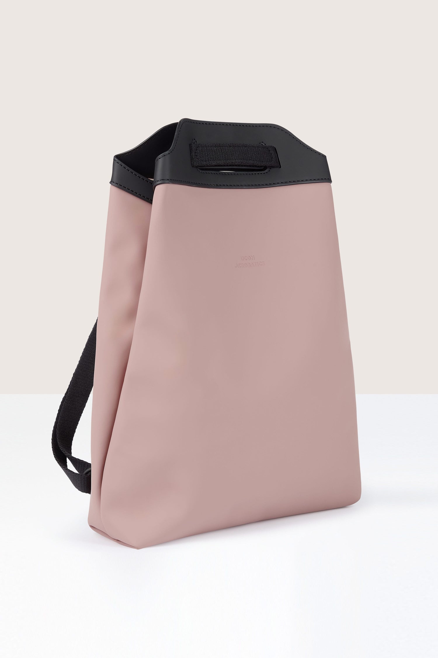 A pink rectangular Una Backpack, crafted from recycled PET bottles, features a black handle and strap. It stands on a white surface against a plain background, showcasing its versatile design.