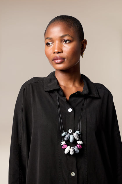 A person with short hair wears a black button-up shirt and the Dotty Two Strand Necklace, featuring large disc beads, while looking slightly to the side against a plain background.