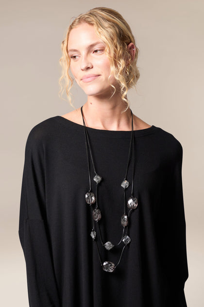 A woman with a dramatic flair wearing a black top and the Silver Leaf Pebble Necklace.